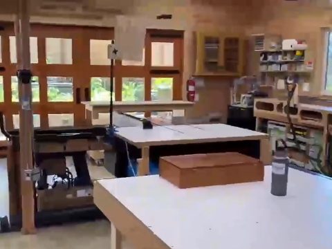 Inside the workshop: assembly tables, a table saw and wall-length workbenches under big windows