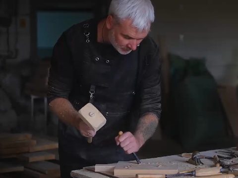 Ted McGrath carving a board with a mallet and chisel at his workbench
