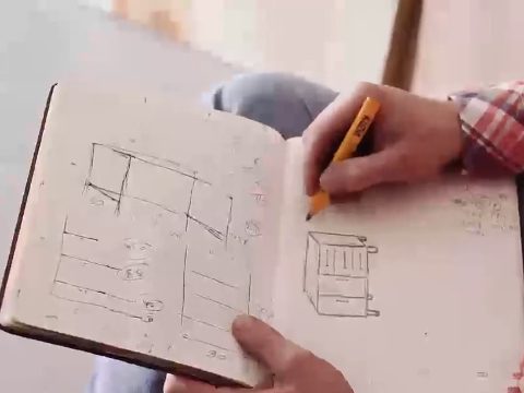 A hand sketching a two-drawer cabinet in pencil in a notebook